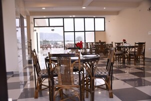 Comedor con sillas y mesas de mimbre, ventanas amplias con vistas a la montaña y piso a cuadros.