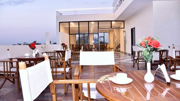 An outdoor dining area with wooden tables and chairs, a glass-enclosed dining room in the background, and a view of the city skyline. - Hotel Saif Ranthambore (Sawai Madhopur)
