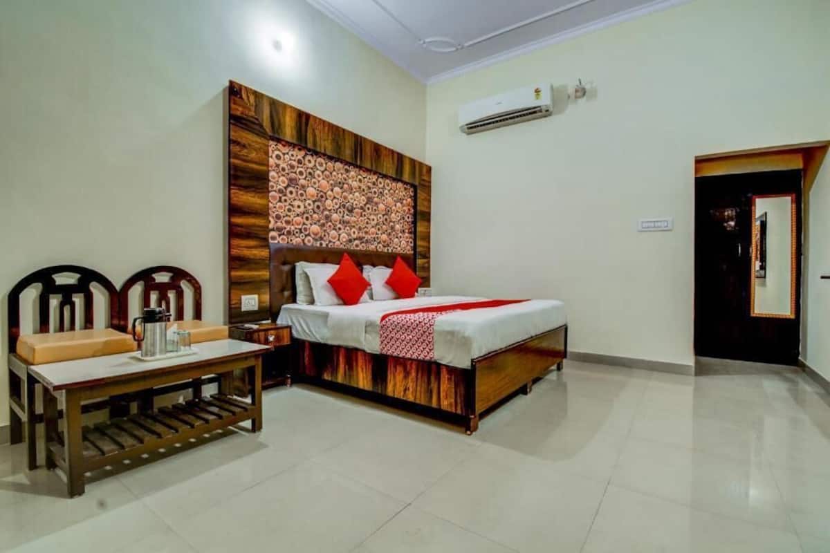 A hotel room with a bed, a bedside table, a chair, and an air conditioning unit on the wall.