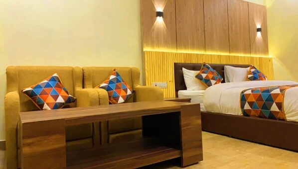 Une chambre d’hôtel comprenant un canapé, un lit, une table basse en bois et une tête de lit dotée d’un éclairage intégré.