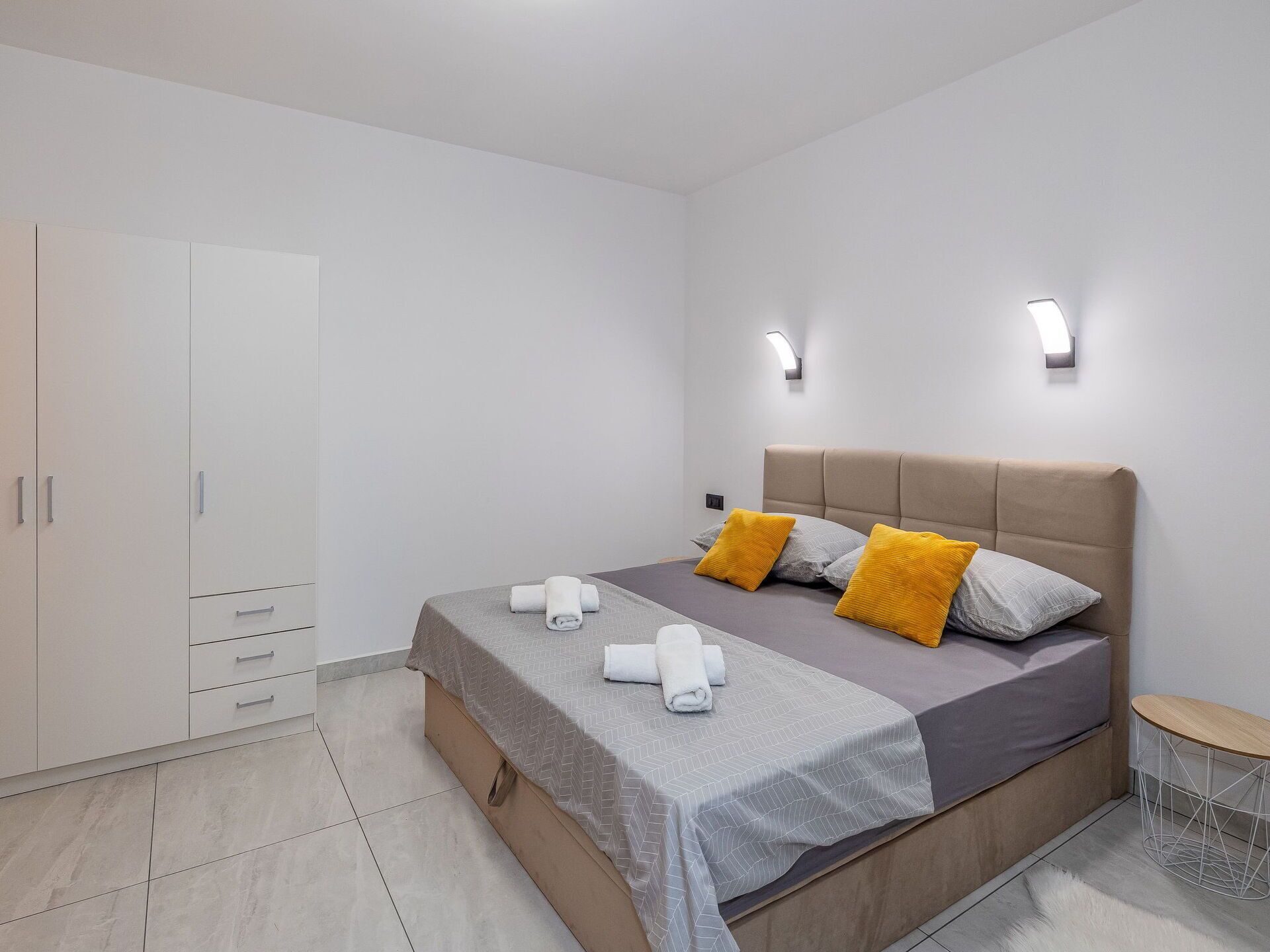 Un dormitorio moderno con cama, armario y dos luces fijadas a la pared.