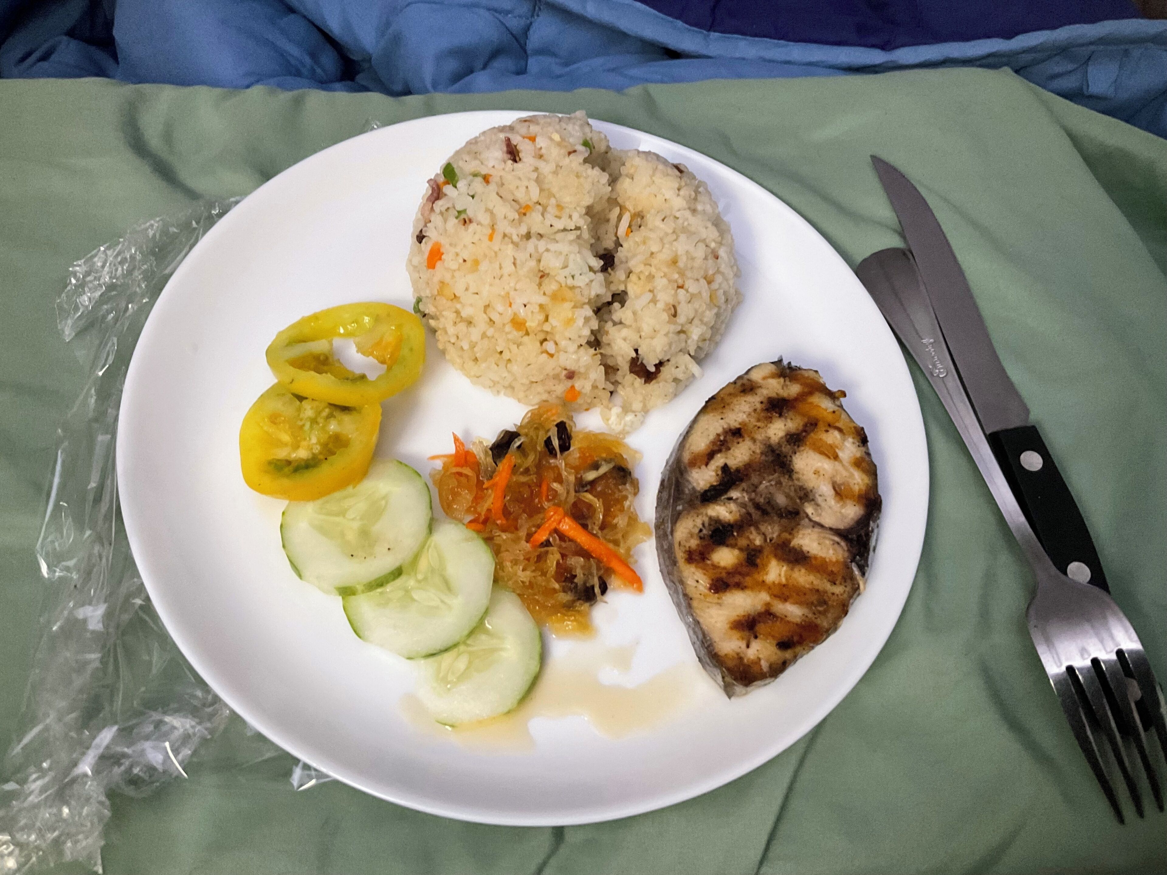 Un plato de arroz, pollo a la parrilla, rodajas de pepino y verduras encurtidas sobre un mantel verde.