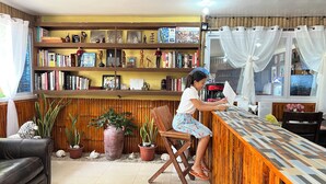 A cozy living room with a wooden bookshelf, a coffee machine, and a window with curtains. - Treasure Beach Co.  (Carles)