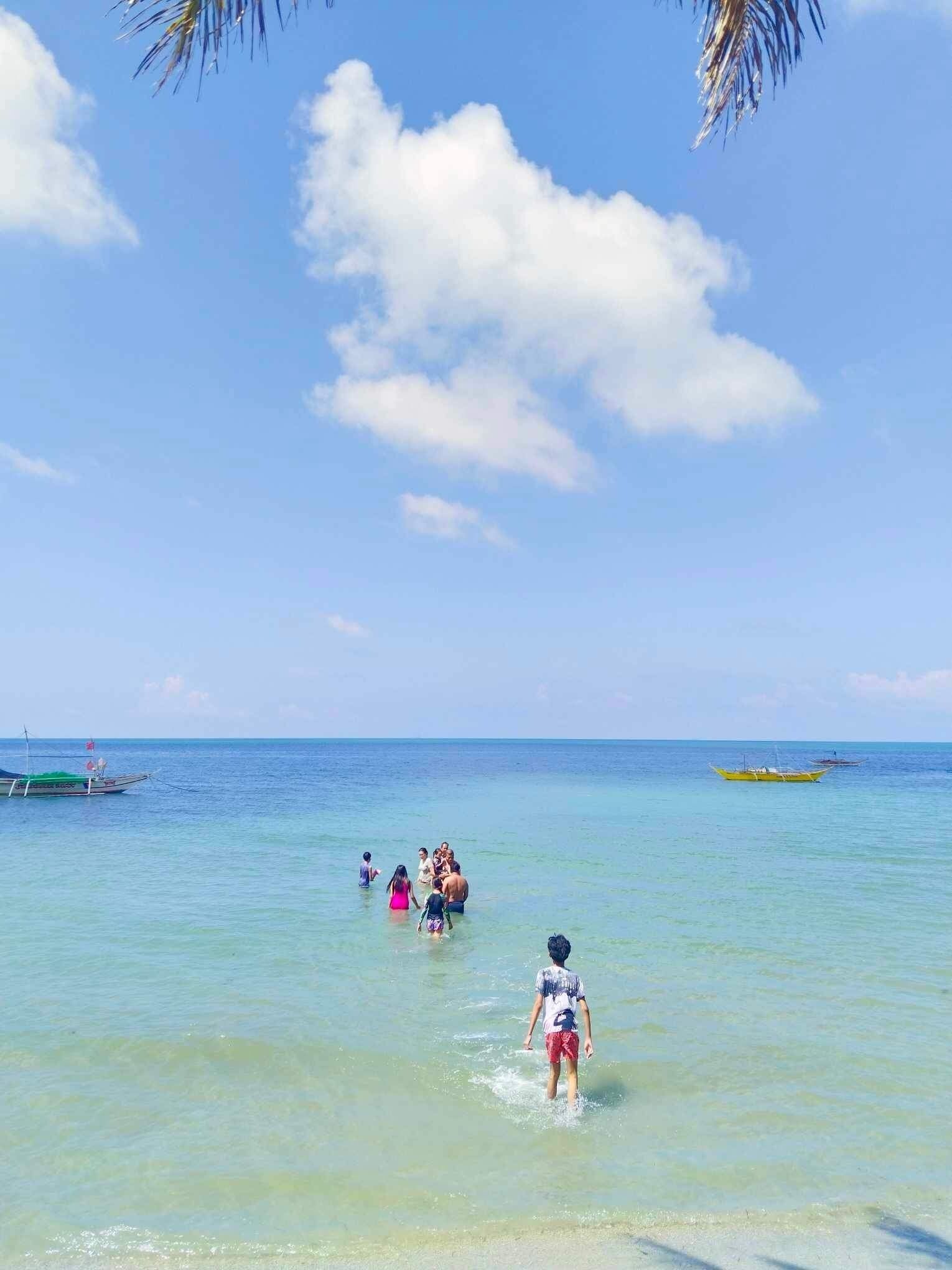 A beach scene with clear water, boats, and people in the water.