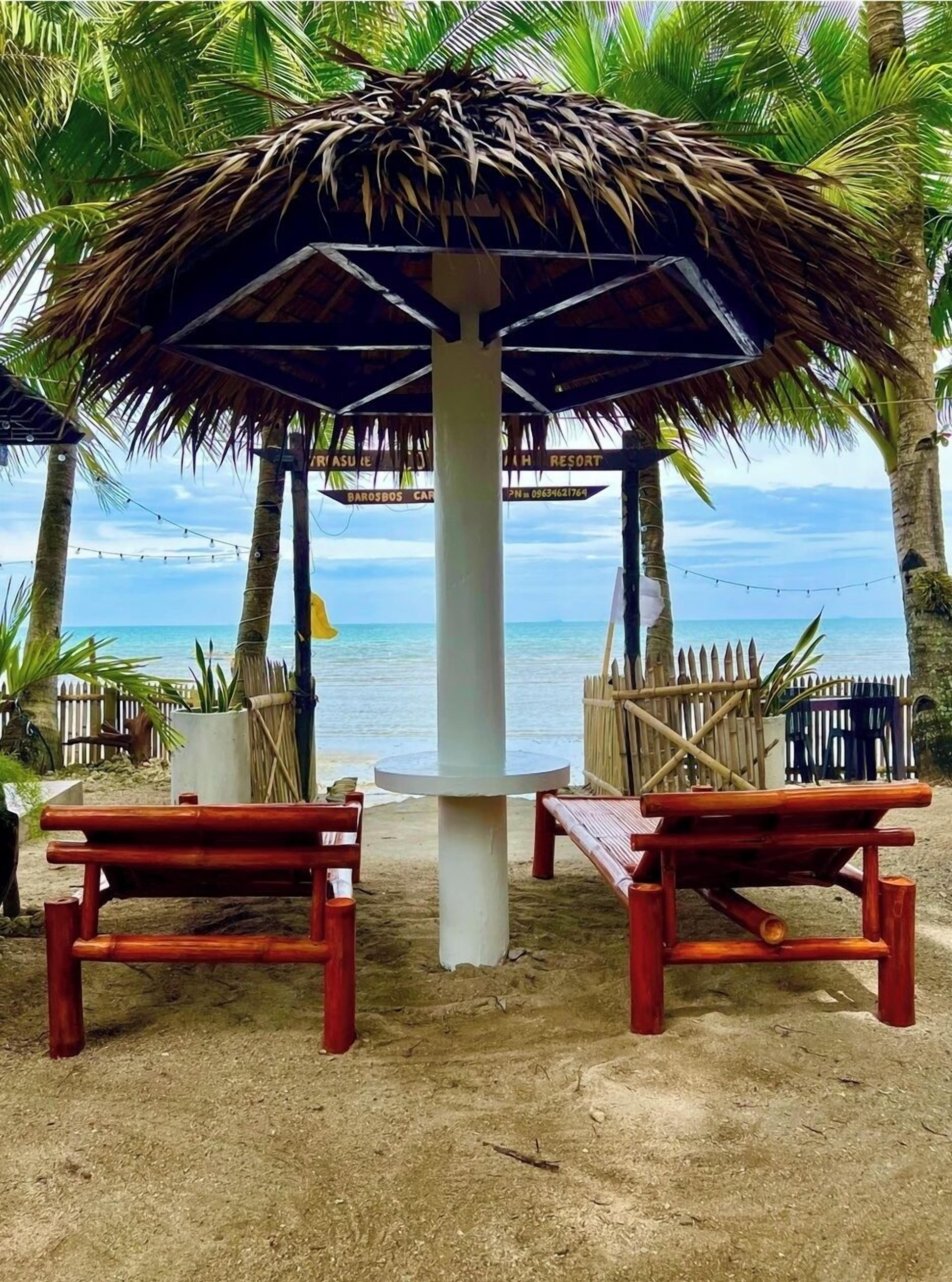 A beach hut with a thatched roof, two wooden benches, and a view of the sea.