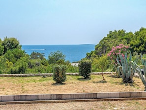 A coastal landscape with a view of the sea, a stone wall, and various plants.
