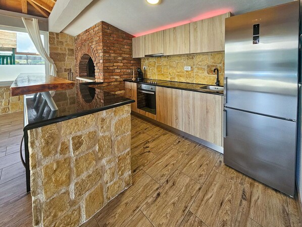 A kitchen with a stone island, wooden cabinets, a stainless steel refrigerator, and a brick oven.