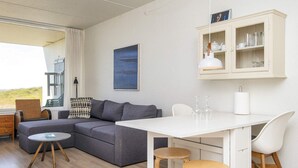 A modern living room with a grey sofa, a white dining table with two stools, and a cabinet with glass doors. - 3 Person Holiday Home in Fano-by Traum (Fano)