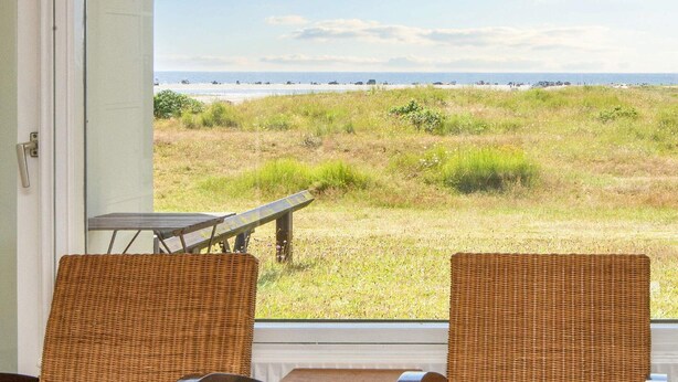 A room with wicker chairs and a table, overlooking a grassy area with a view of the beach and ocean. - 3 Person Holiday Home in Fano-by Traum (Fano)