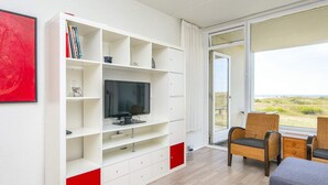 A modern living room with a flat-screen TV, a bookshelf, and a view of the outdoors. - 3 Person Holiday Home in Fano-by Traum (Fano)