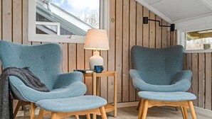 A room with two blue armchairs, a small wooden side table with a lamp, and a window with a view of a house. - "Wilmer" - 600m from the sea by Interhome (Løkken)