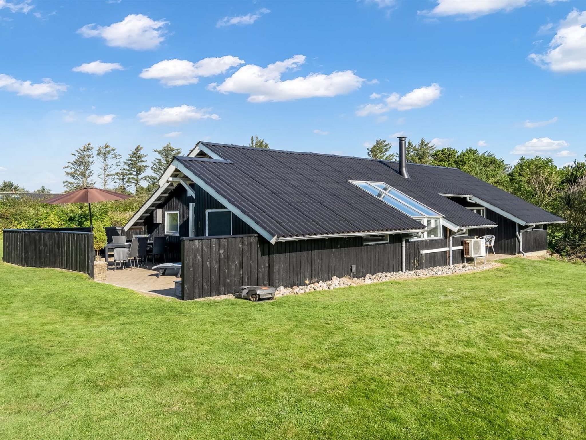 A modern house with a sloped roof, large windows, and a fenced backyard.