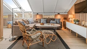 A cozy, well-lit room with a large window, a comfortable sofa, a wicker chair, and a small table with candles. - "Wilmer" - 600m from the sea by Interhome (Løkken)