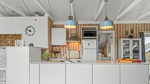 A modern kitchen with white cabinetry, a built-in clock, pendant lights, and a wooden accent wall. - "Wilmer" - 600m from the sea by Interhome (Løkken)