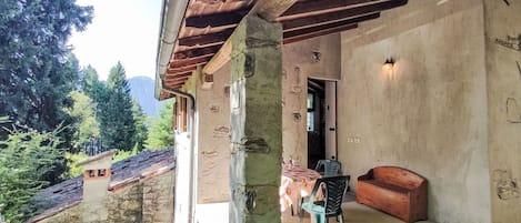 A rustic building with a stone exterior, a wooden porch, and a view of a mountainous landscape.