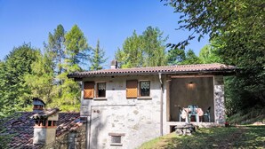 A rustic stone building with a tiled roof, a small balcony, and a table with chairs outside.
