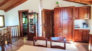 A wooden interior with a dining table, chairs, a cabinet with glassware, and a kitchen area.