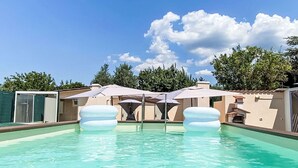 Ein Schwimmbecken mit klarem Wasser, umgeben von Sonnenschirmen und Liegestühlen.