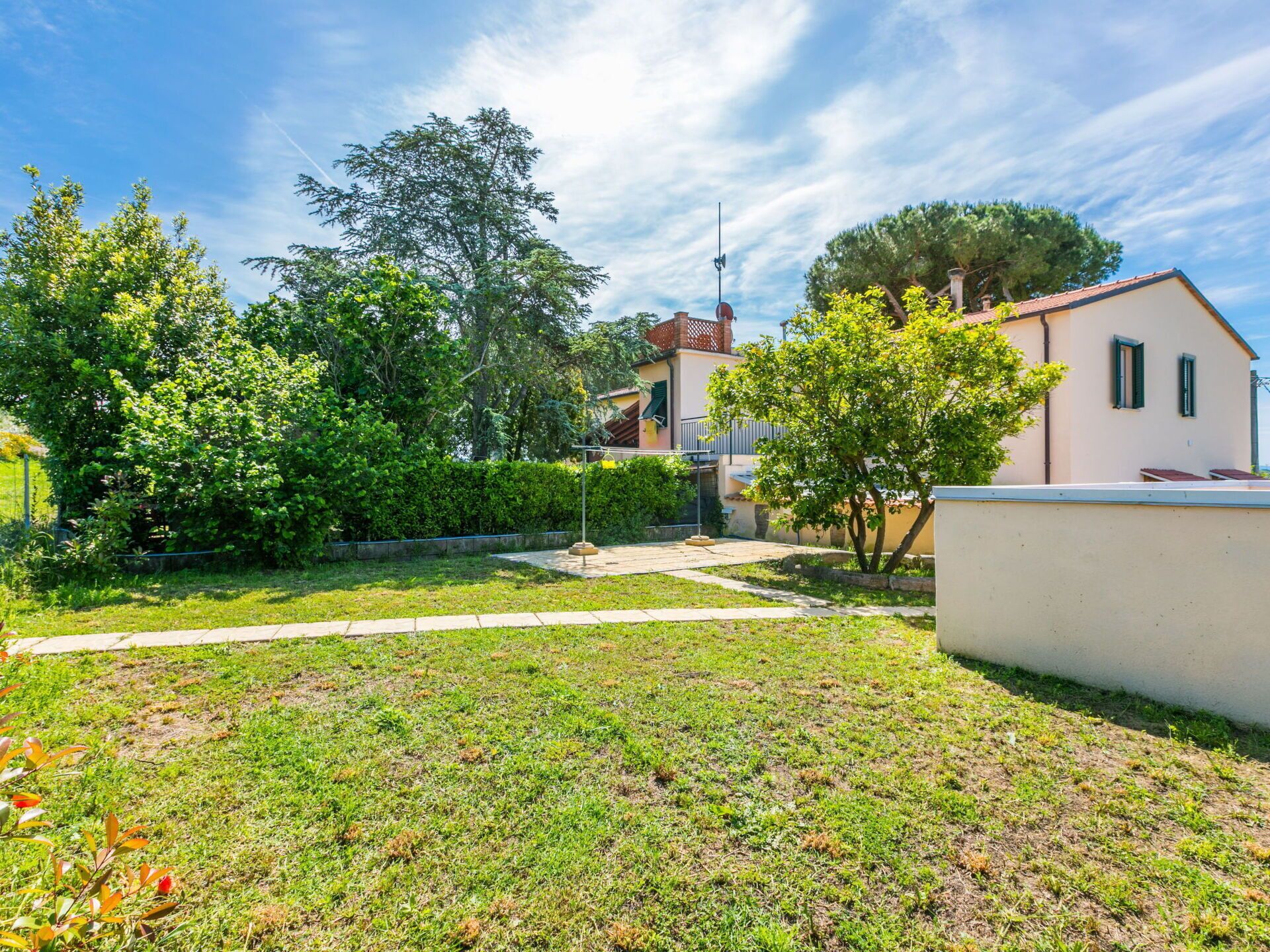 A residential property with a well-maintained lawn, a pathway leading to a house with a tiled roof, and a small garden area with various plants.