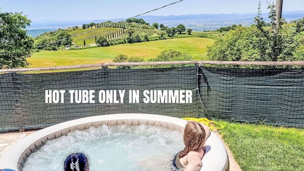 A hot tub with two people in it, surrounded by a grassy area and a view of the countryside. - Beautiful private villa with private pool, WIFI, A/C, hot tub, TV, patio and panoramic view (Scansano)