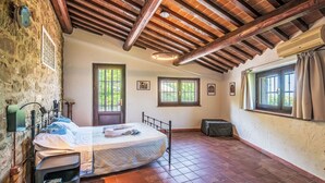 Un dormitorio rústico con techo inclinado, cama, banco y ventana con cortinas.