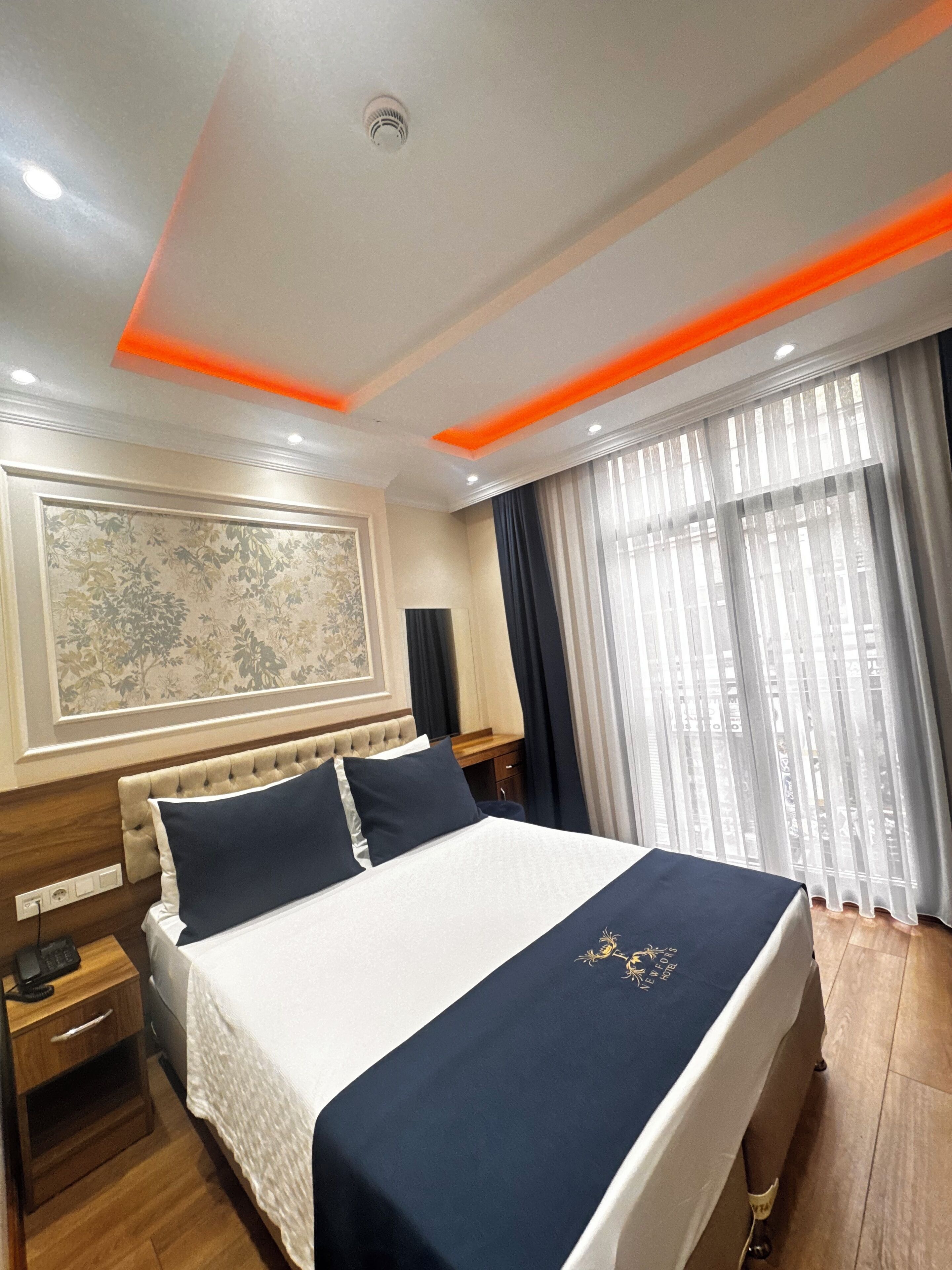 Habitación de hotel con una cama grande, una mesita de noche, un escritorio y una ventana con cortinas.