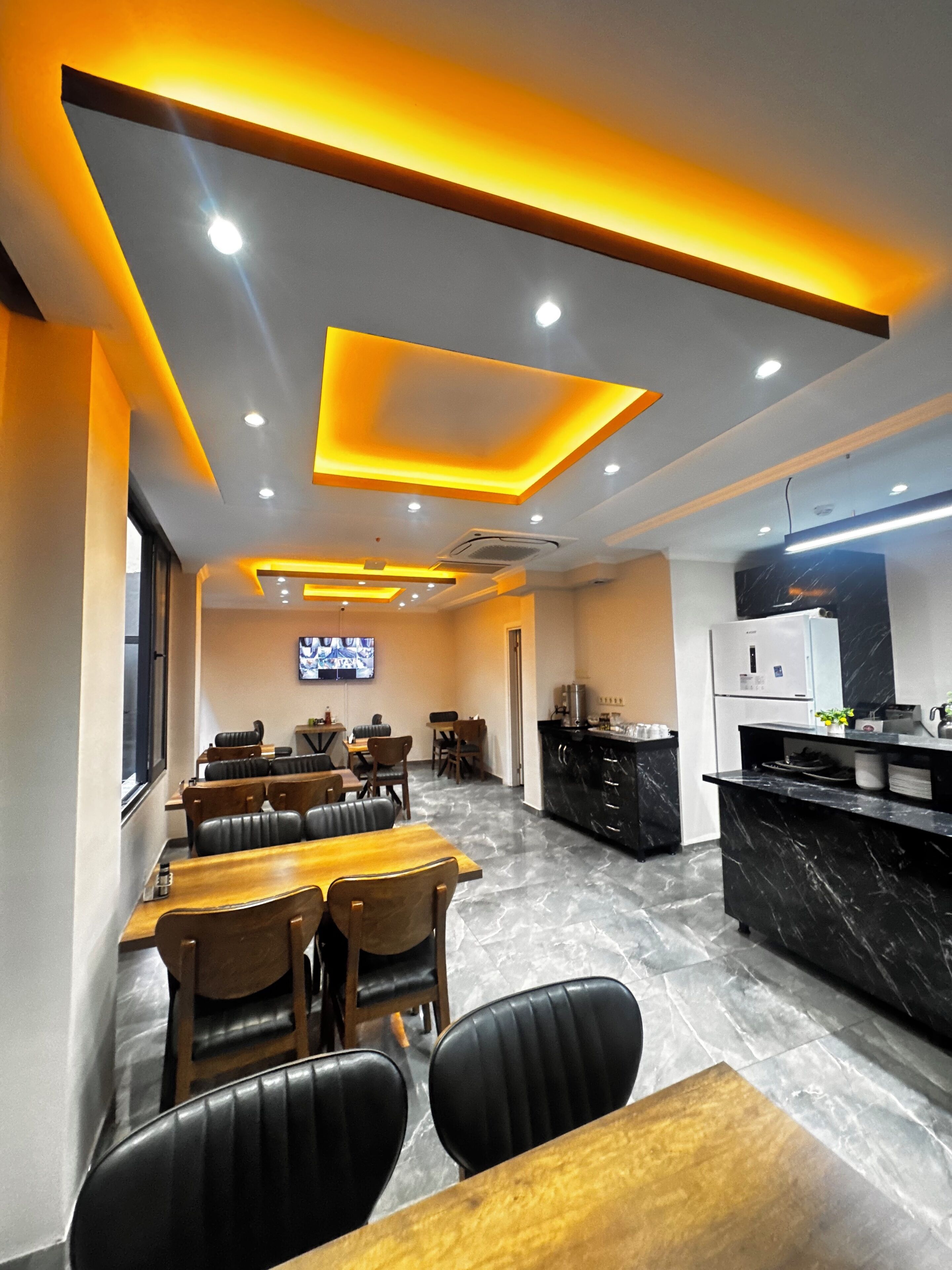 Um restaurante moderno com um balcão comprido, cadeiras de couro preto e uma televisão fixada na parede.