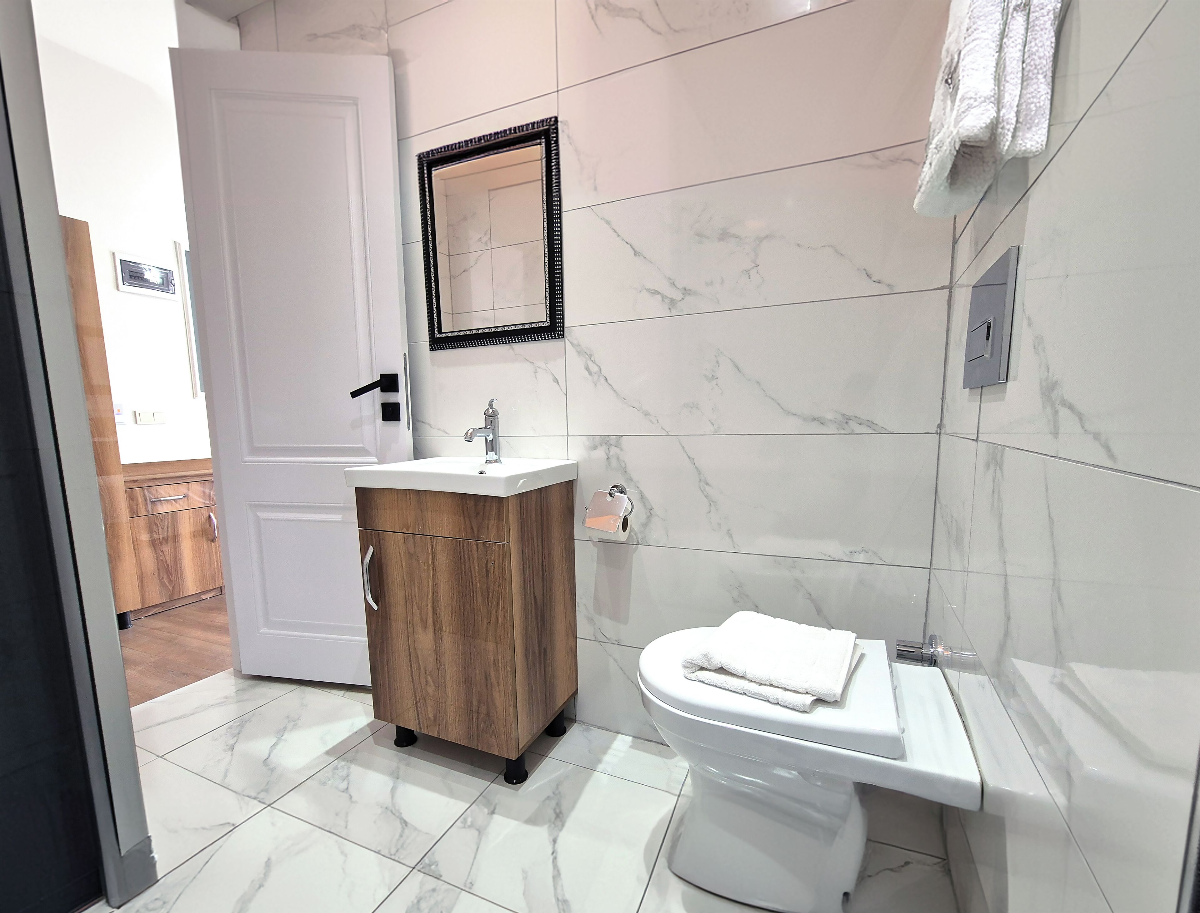 A modern bathroom with a white toilet, a wooden cabinet with a sink, and a mirror above the sink.