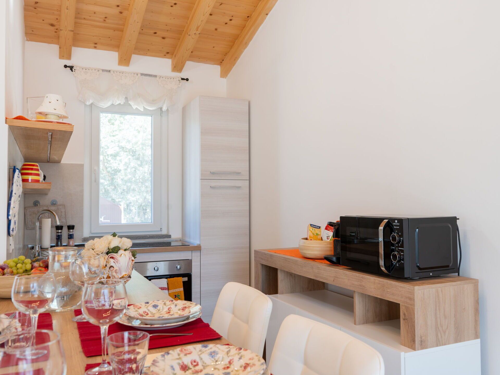 A compact kitchen with a wooden ceiling, a window, and a microwave on a wooden shelf.