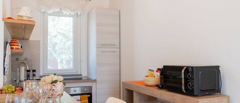 A compact kitchen with a wooden ceiling, a window, and a microwave on a wooden shelf.