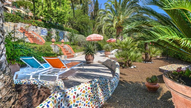 Ein Garten mit Palmen, einer Mosaikwand und Sitzgelegenheiten im Freien.