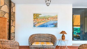 Ein gemütliches Zimmer mit Korbmöbeln, einem Gemälde einer Küstenstadt und einer Steinwand.