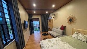 Hotellihuone, jossa on sänky, sohva, seinälle asennettu televisio, puulattia ja ikkunasta avautuva näkymä ulos.