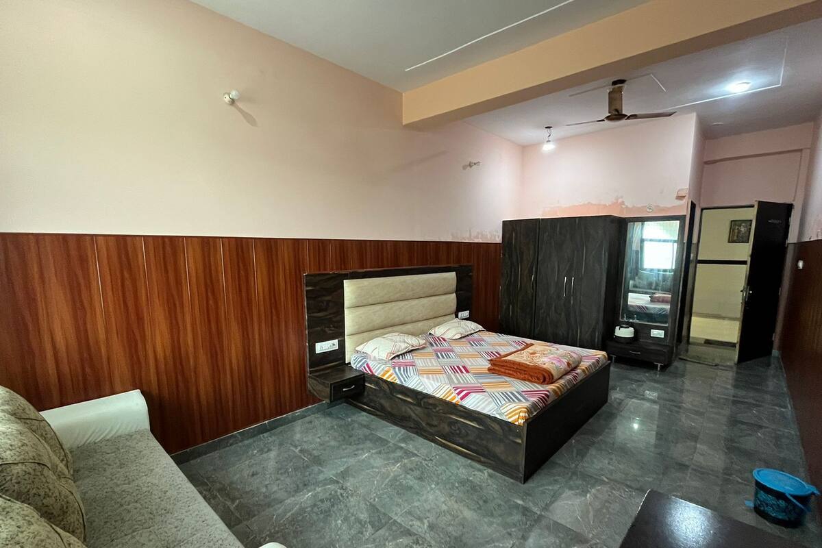 A bedroom with a bed, a wardrobe, a wardrobe mirror, a sofa, and a small table.