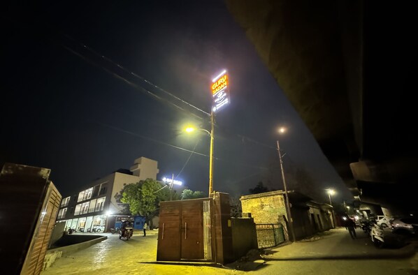 A nighttime street scene with a prominent sign for "Guru Sadan" and a building with multiple stories in the background. - Guru Sadan | A Luxe Stay (Faizabad)