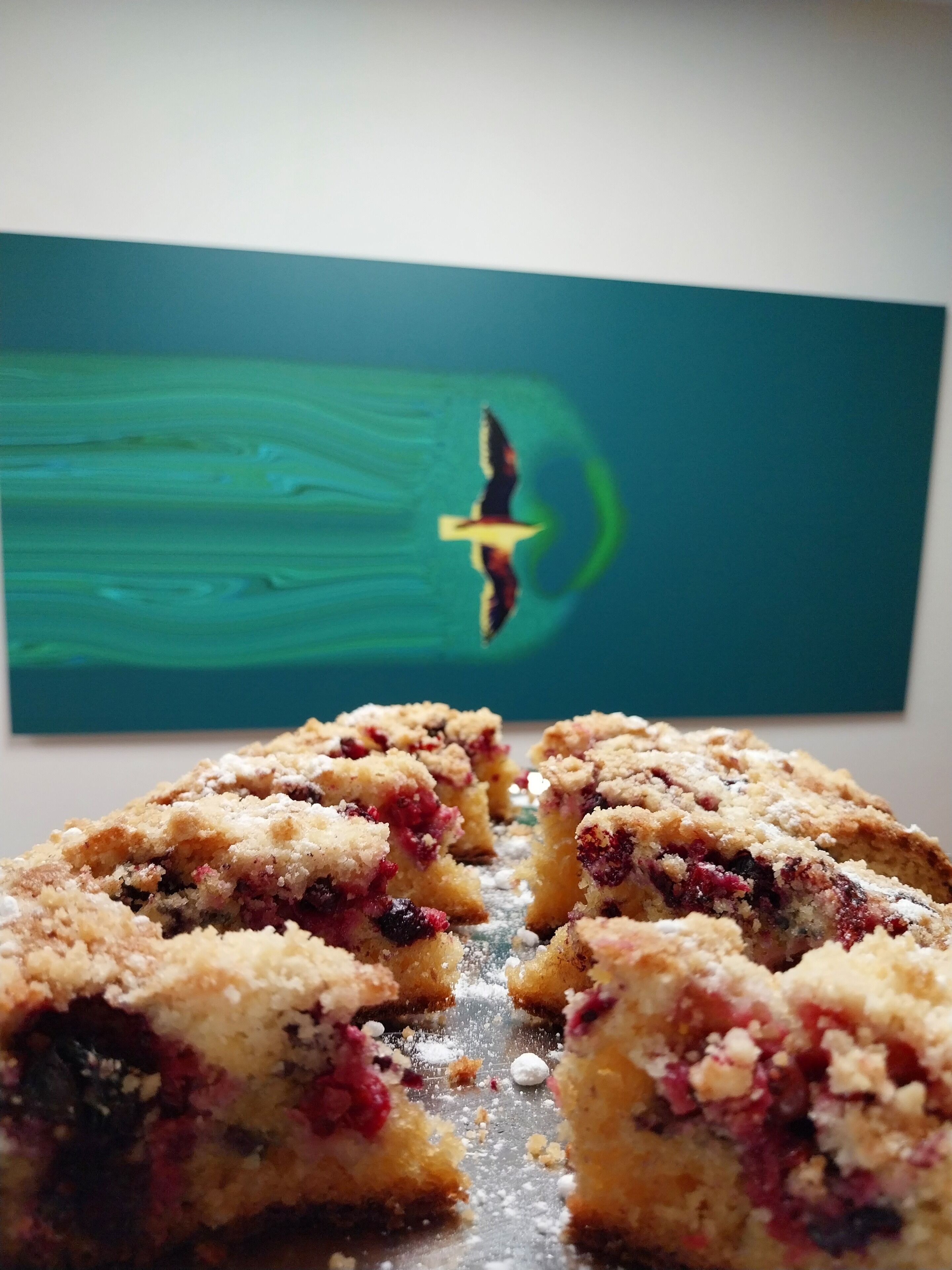 A close-up of a dessert with a crumbly topping, possibly a berry crumble, with a bird in flight on a green background.