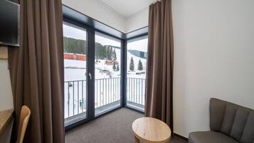 Et værelse med balkon, sofa, lille rundt bord og gardiner.