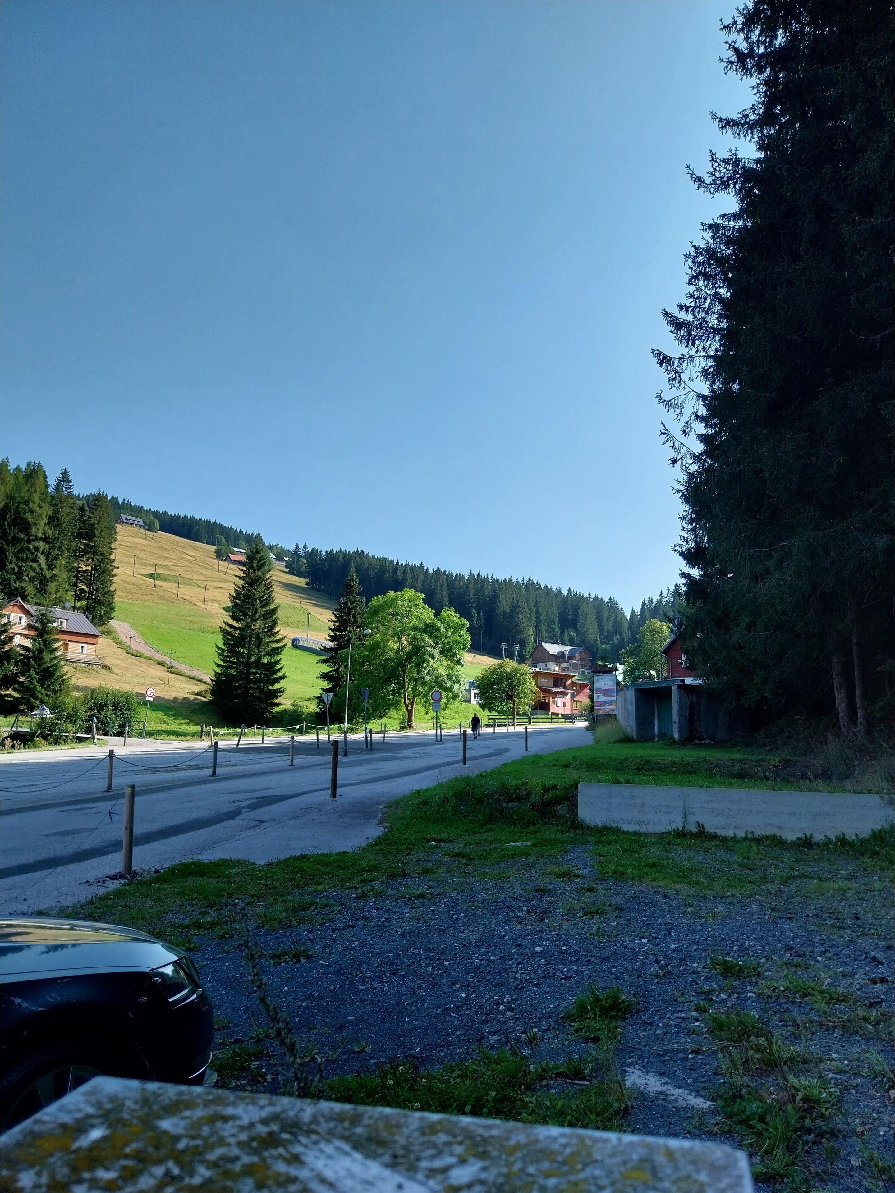 A rural road with houses on the side, surrounded by greenery and hills.