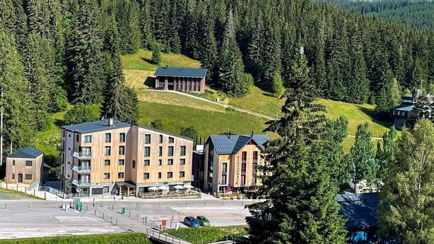 A modern hotel with multiple buildings, a parking area, and a mountainous backdrop. - Hotel Zelený Potok (Pec pod Snezkou)