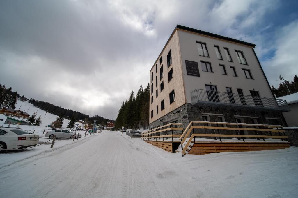 A multi-story building with a stone base and a flat roof, surrounded by snow-covered ground and parked cars.