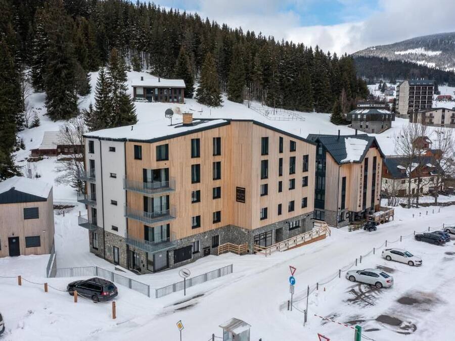 A modern multi-story building with a mix of wooden and stone facades, surrounded by snow-covered landscape and trees.