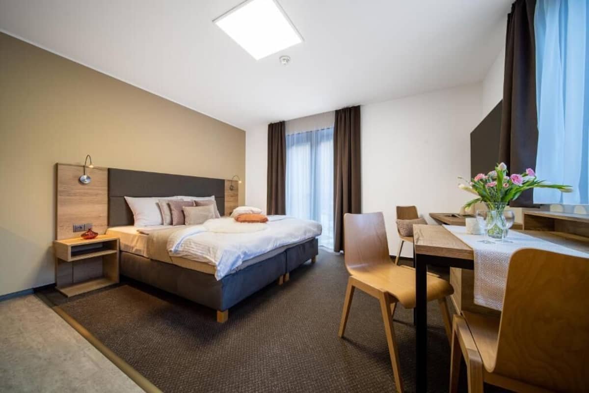 Una habitación de hotel moderna con una cama, una mesita de noche, una silla y un escritorio pequeño con un florero.