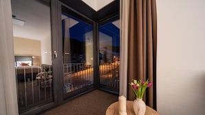 A hotel room with a sliding glass door leading to a balcony, a round wooden table with candles and a vase of flowers, and a view of the cityscape at night. - Hotel Zelený Potok (Pec pod Snezkou)