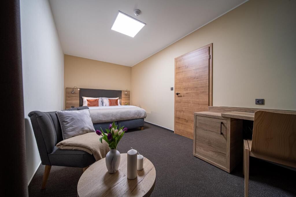 Ein gemütliches Hotelzimmer mit Bett, Schreibtisch, Stuhl und einem kleinen Tisch mit Blumen.