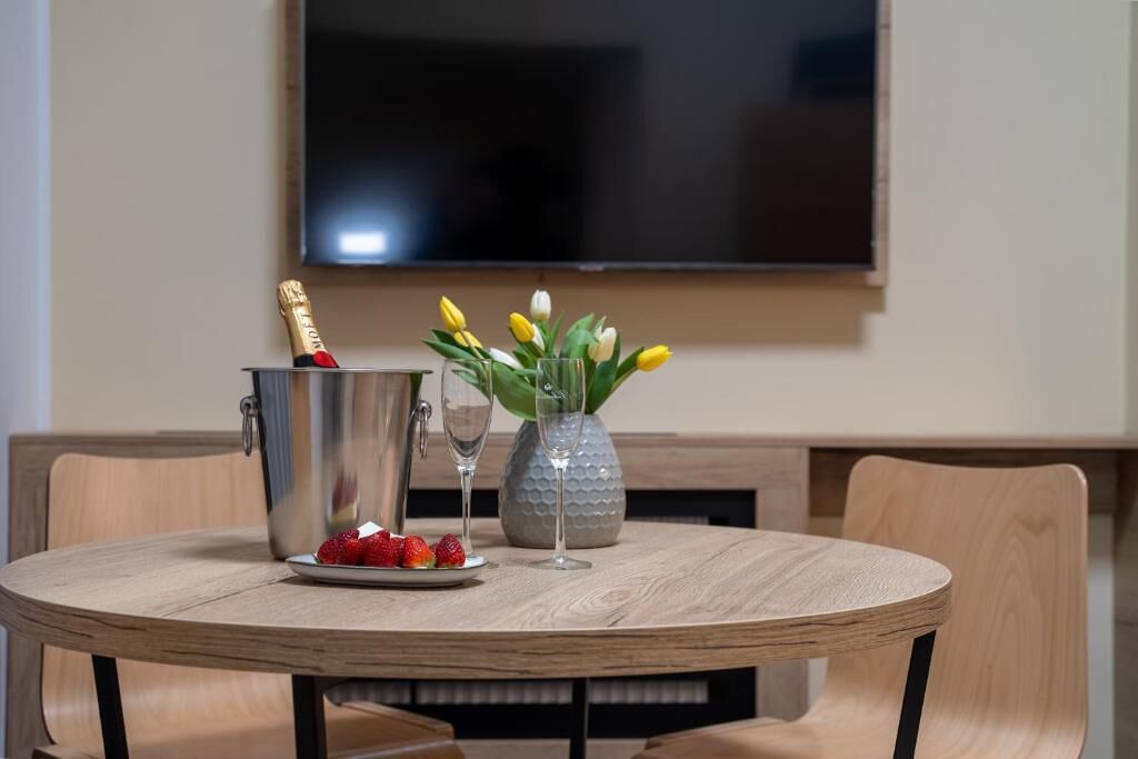 Une table ronde en bois, sur laquelle se trouvent une bouteille de champagne, un verre et un vase rempli de tulipes jaunes.