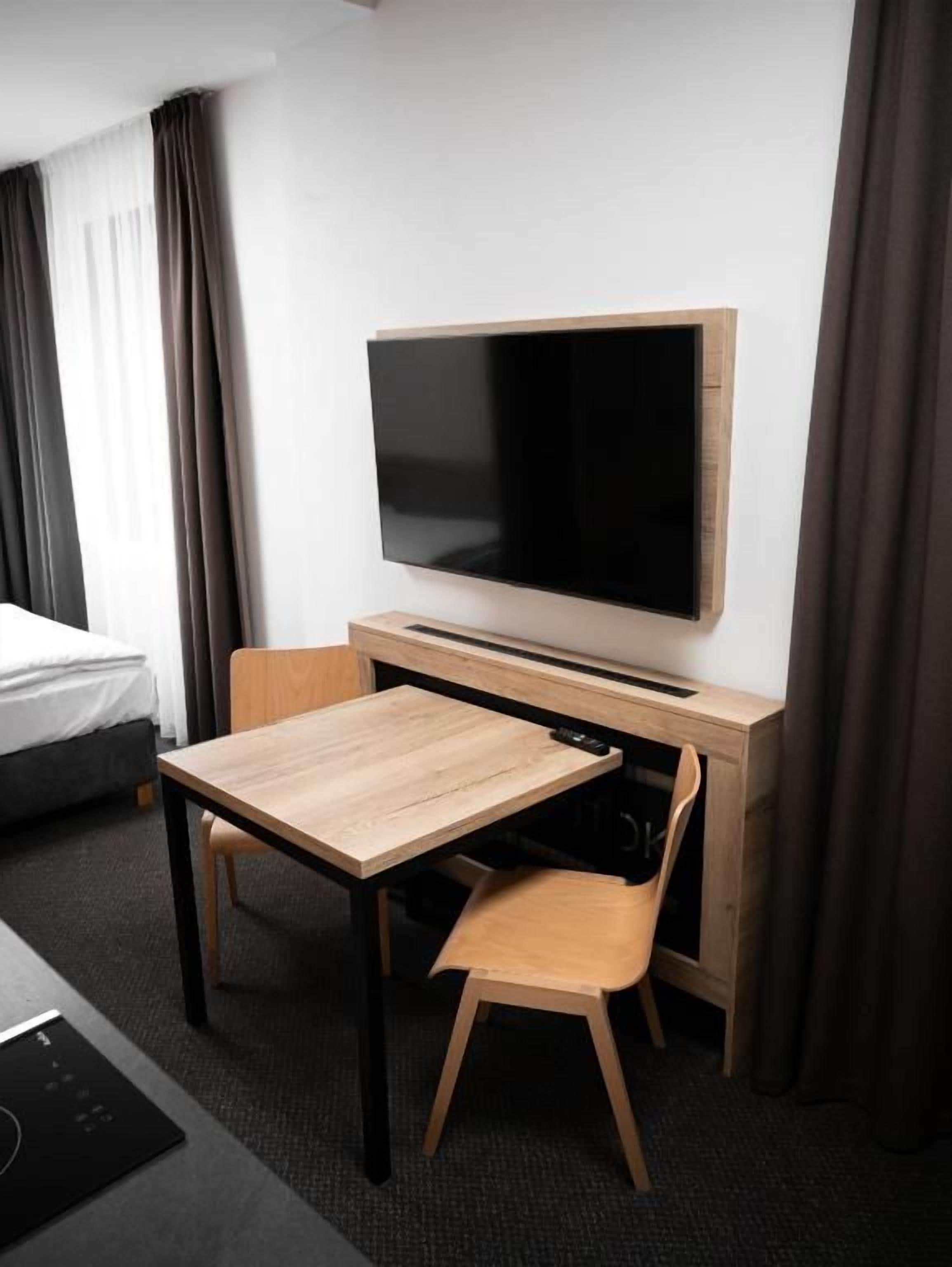 Habitación de hotel con cama, escritorio con silla, televisor de pantalla plana y ventana con cortinas.