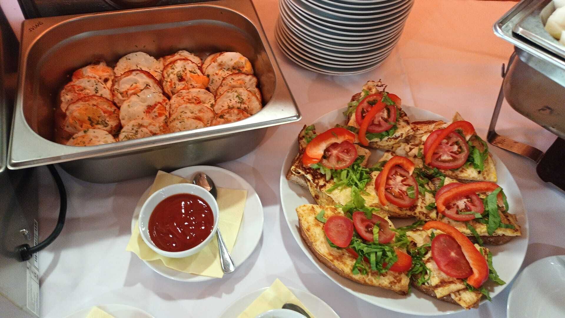 A buffet table with a variety of food items including sliced meat, grilled chicken sandwiches, and a bowl of red sauce.