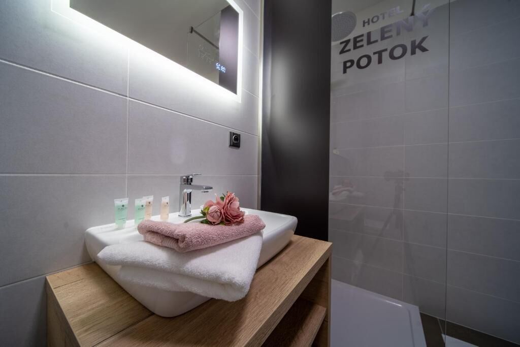 Et moderne badeværelse med en hvid vask, træbordplade og et spejl over. Der er håndklæder og toiletartikler på vasken.
