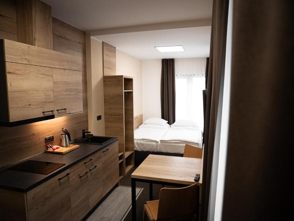 A compact hotel room with a kitchenette, a bed, and a small dining area.