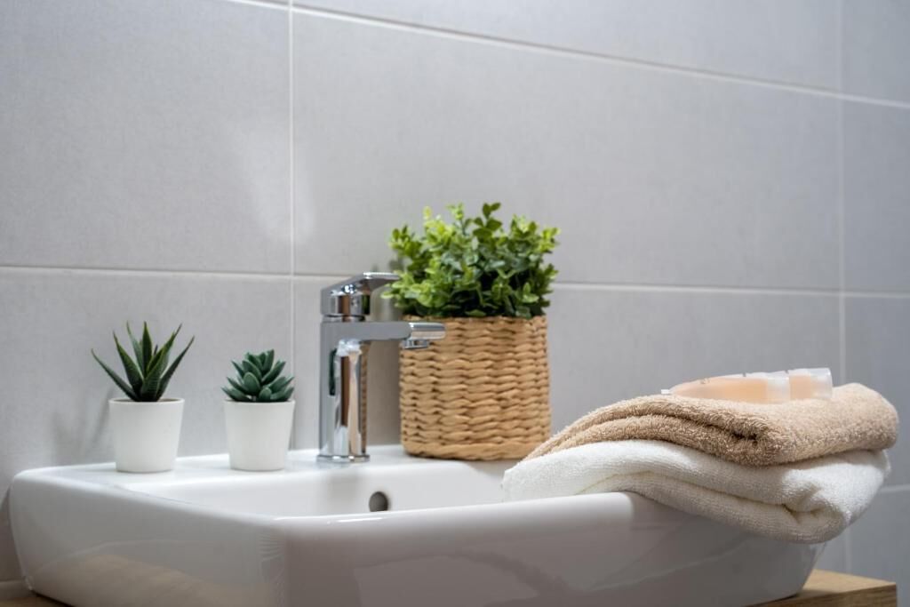 Un lavamanos de baño con dos plantas en macetas, una cesta tejida y una pila de toallas.